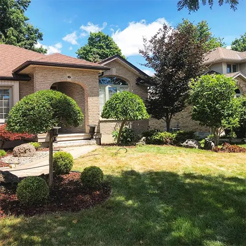 A tidy front garden of shaped evergreens and rounded shrubs beside a brick house.